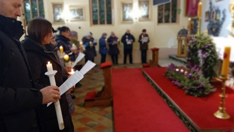 Wierni ze świecami podczas nabożeństwa, przy ołtarzu kwiatowa dekoracja